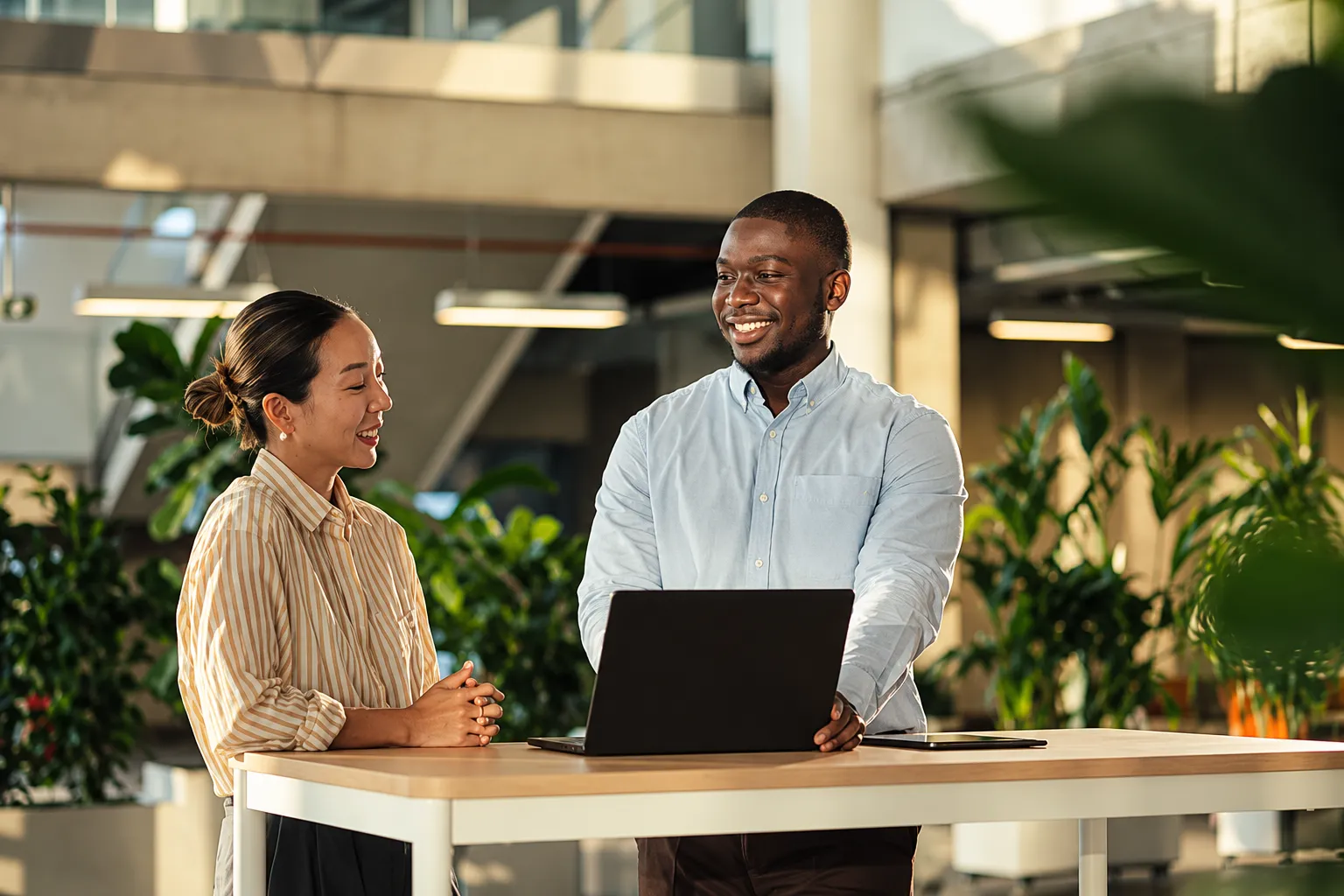 Two colleagues talking beside a laptop in an office with plants