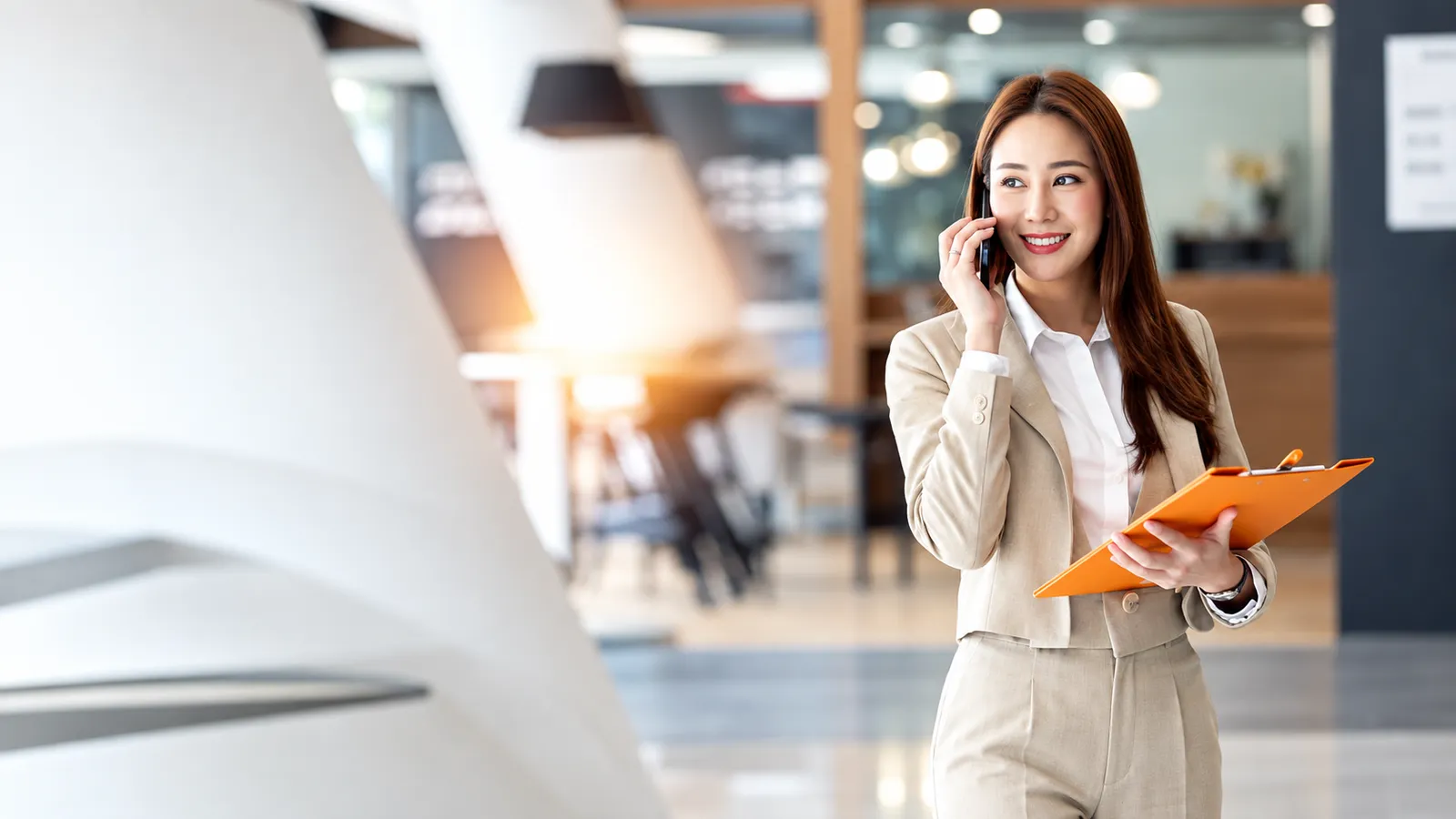 A professional taking a phone call while holding a clipboard in a bright office