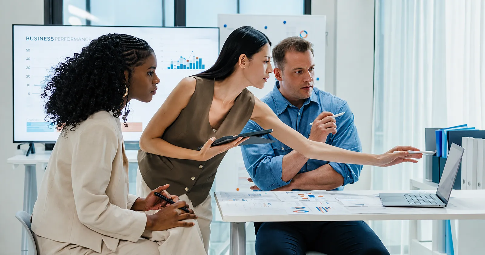 Three colleagues reviewing charts and working information on an office monitor