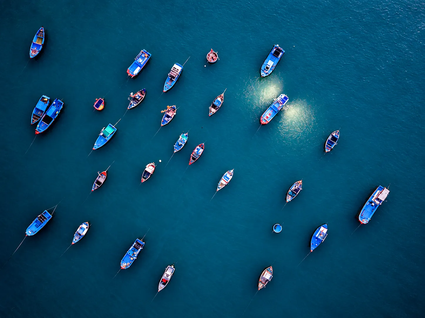 Aerial view of blue fishing boats moored on dark teal water off the Vietnam coast