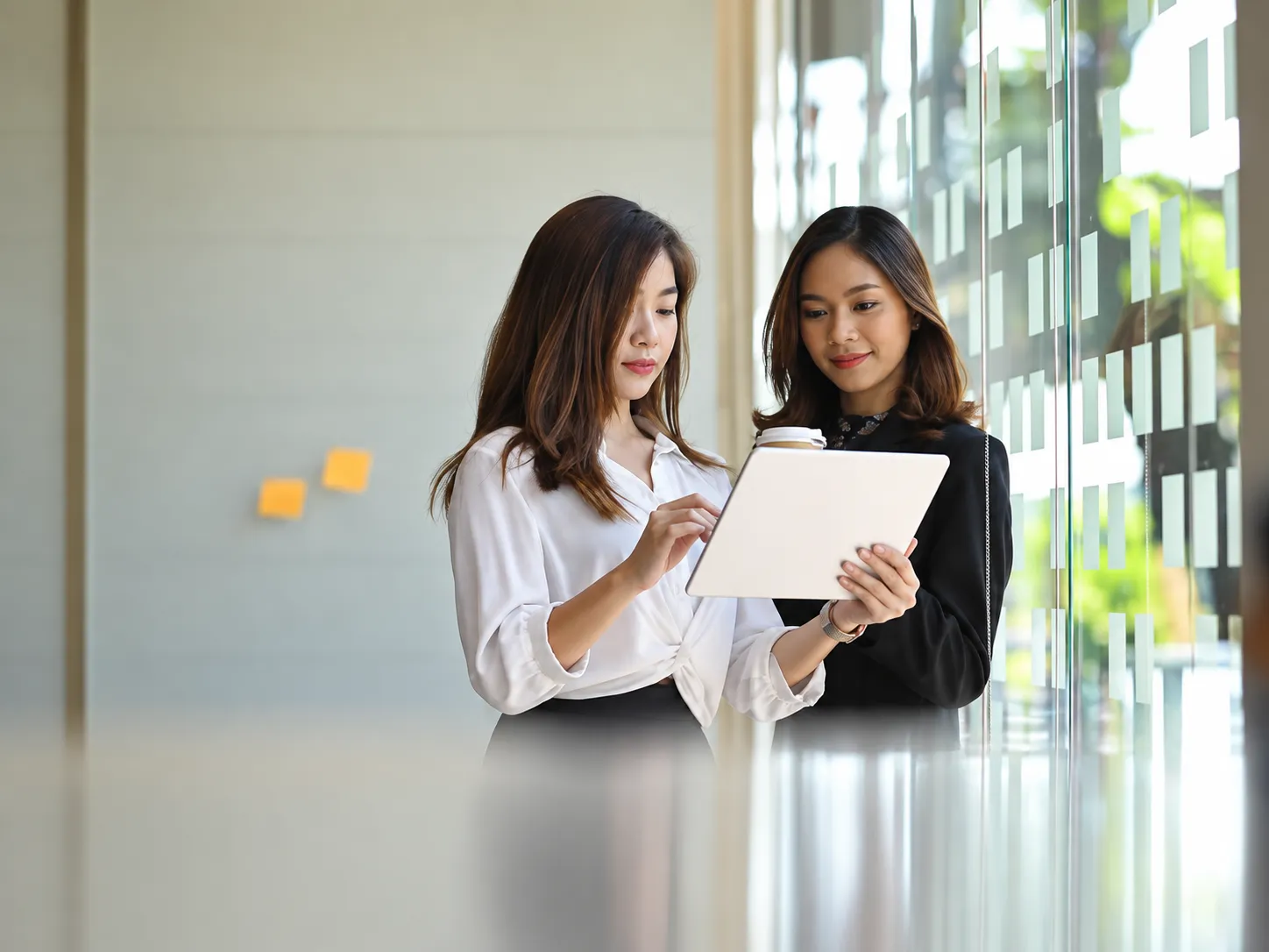 Two colleagues reviewing information together beside an office window