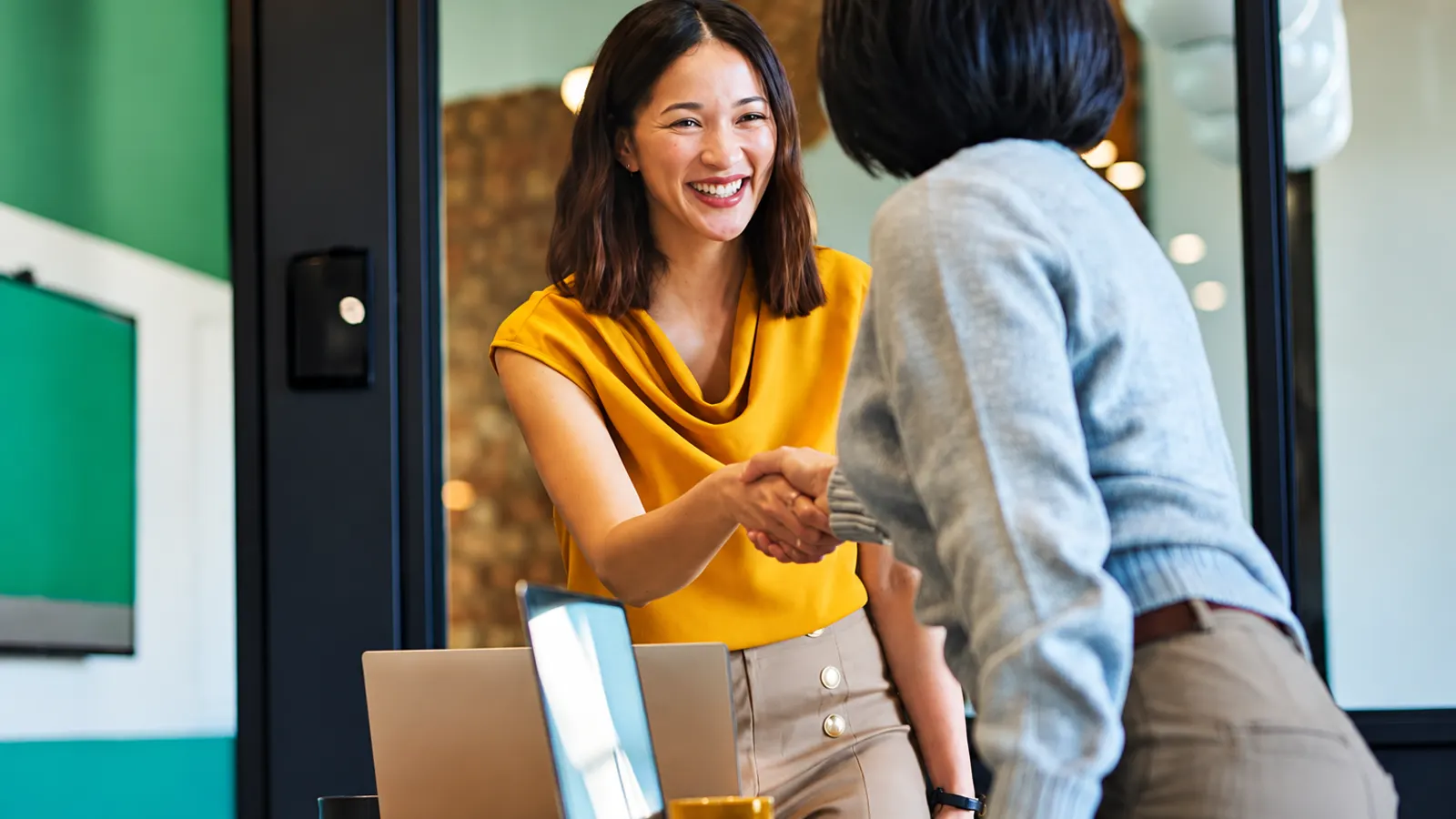 A smiling professional shaking hands with a new colleague across a desk